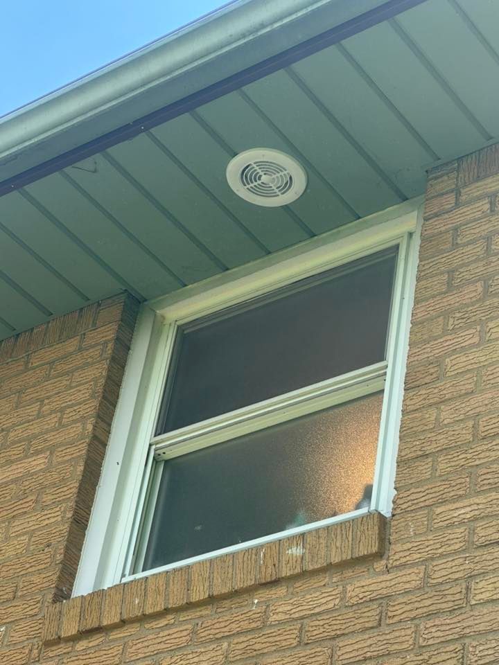 Brick building exterior with a window and a ceiling vent. The ceiling is teal and the window has a white frame.