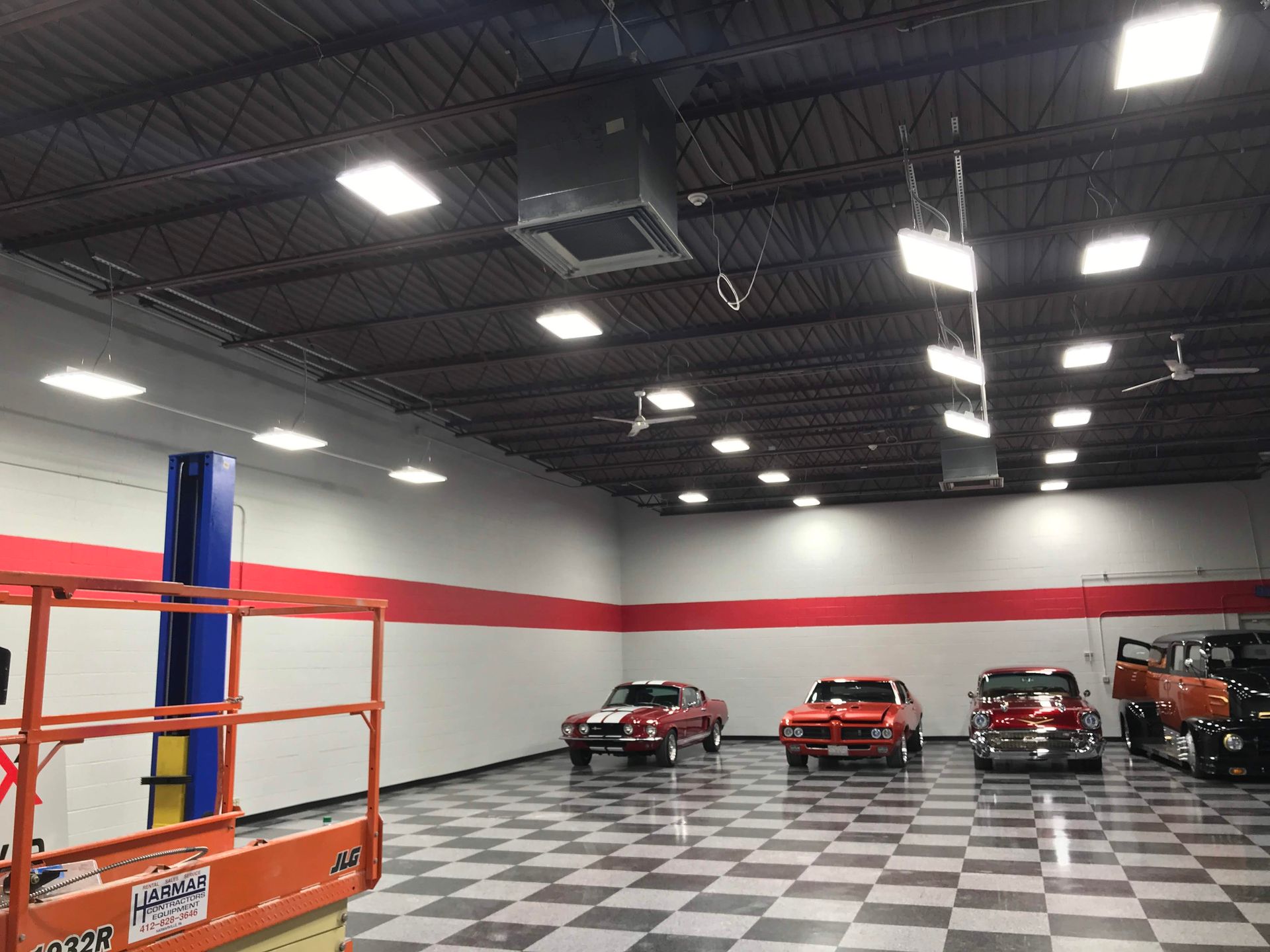 A man with a beard in a yellow shirt works with wires in a basement. He is kneeling and holding a small, blue box.