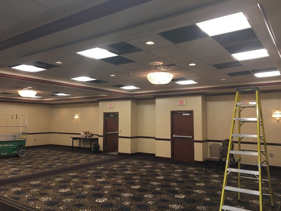 A man in a yellow shirt works on an electrical panel in a room with wood paneling.