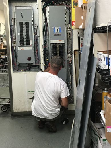 A man working on an electrical panel in a commercial setting.
