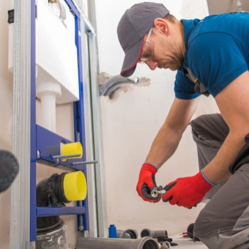 A plumber is working on a toilet in a bathroom.