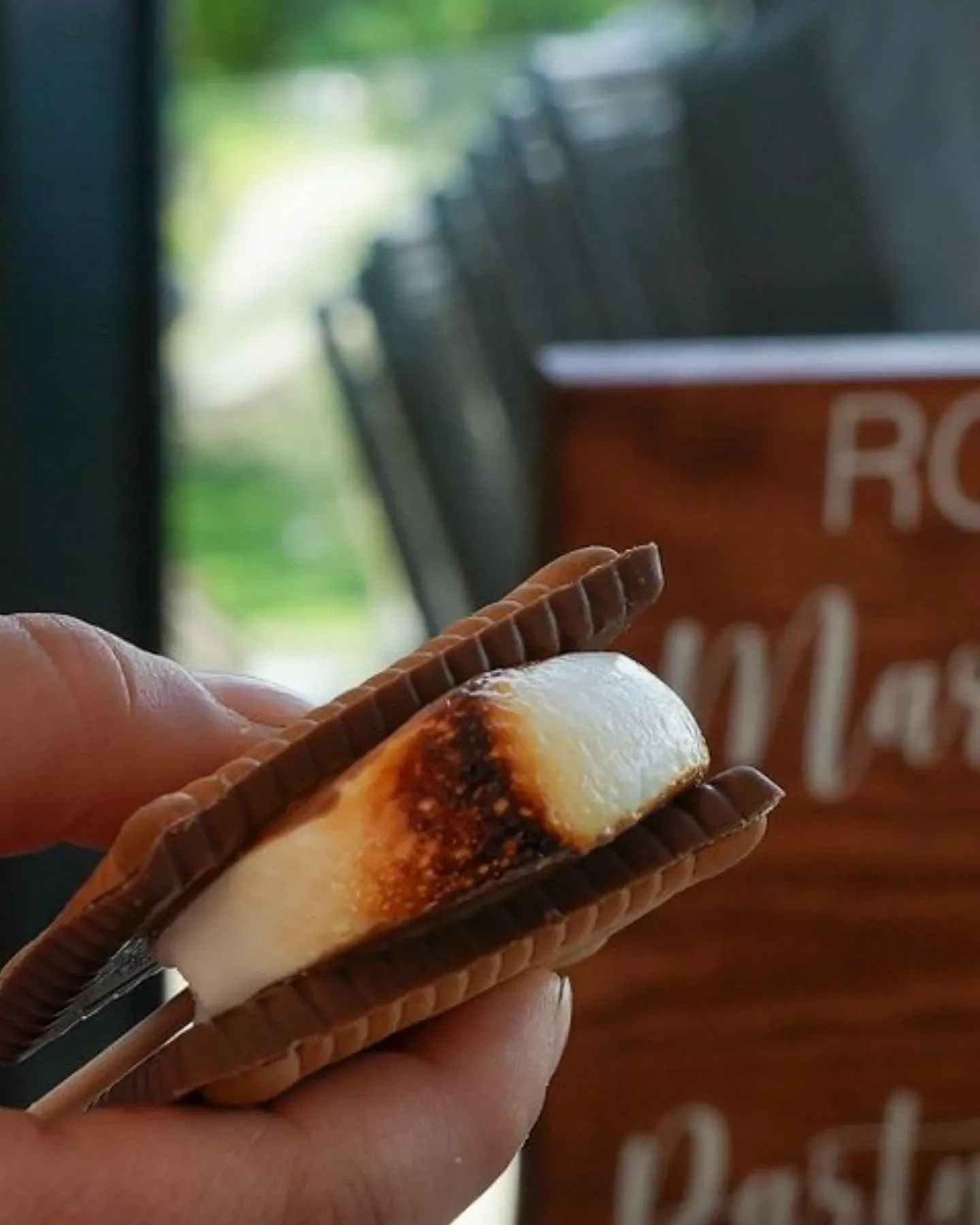 A person is holding a s'mores sandwich in front of a sign that says roasted marshmallows