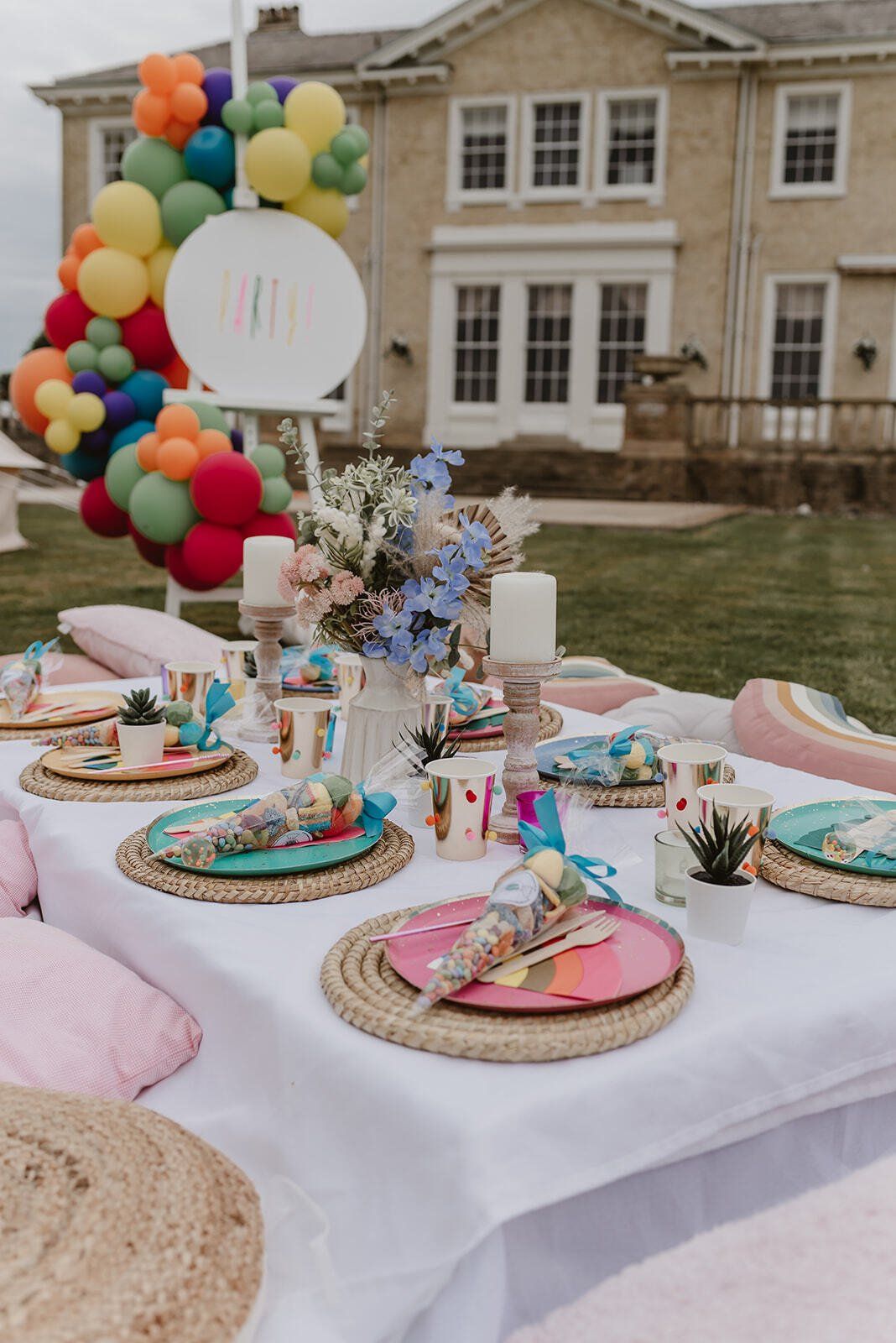 A table with plates , cups , and balloons on it in front of a house.
