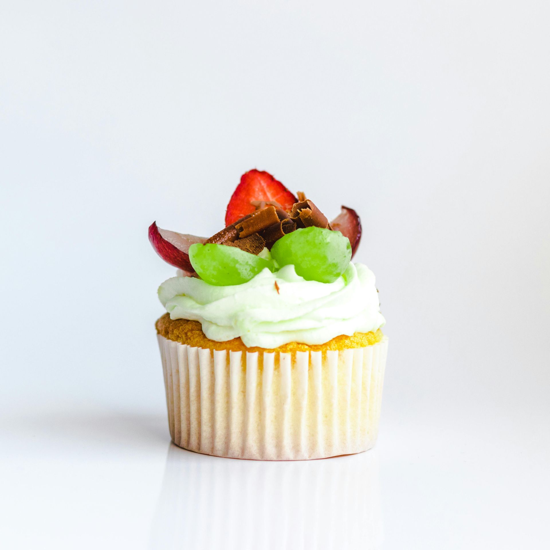 A cupcake with whipped cream and fruit on top on a white surface.