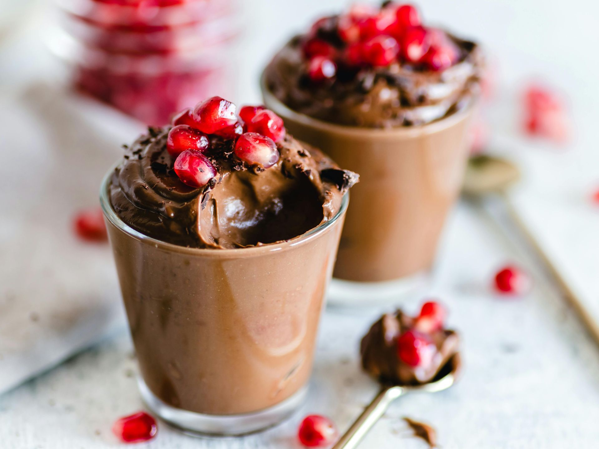 Two cups of chocolate mousse with pomegranate seeds on top.