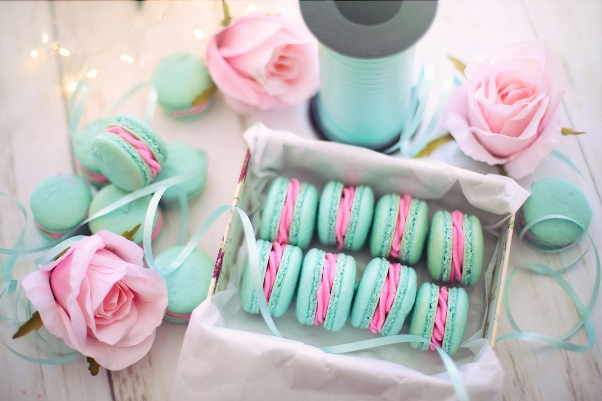 A box of macarons with pink ribbon and roses on a table.