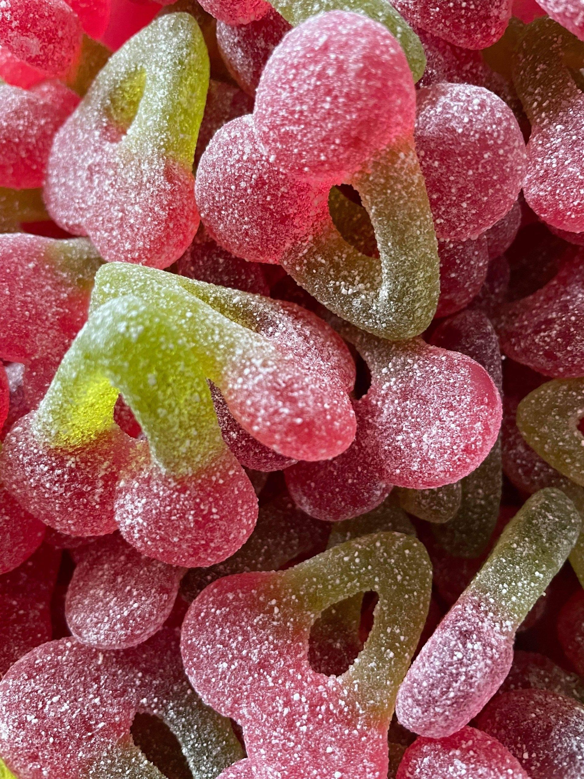 A pile of pink and green gummy cherries with holes in them.
