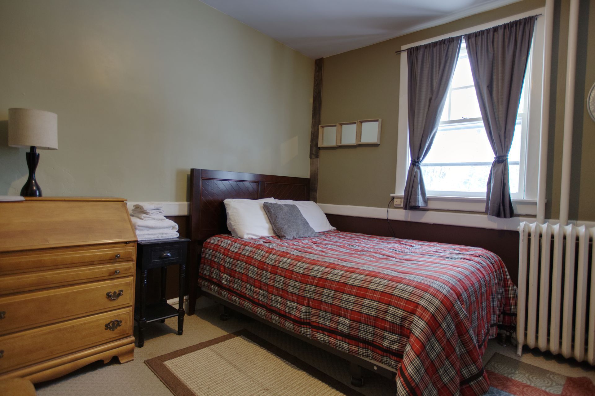 A bedroom with a bed , dresser , lamp and radiator.