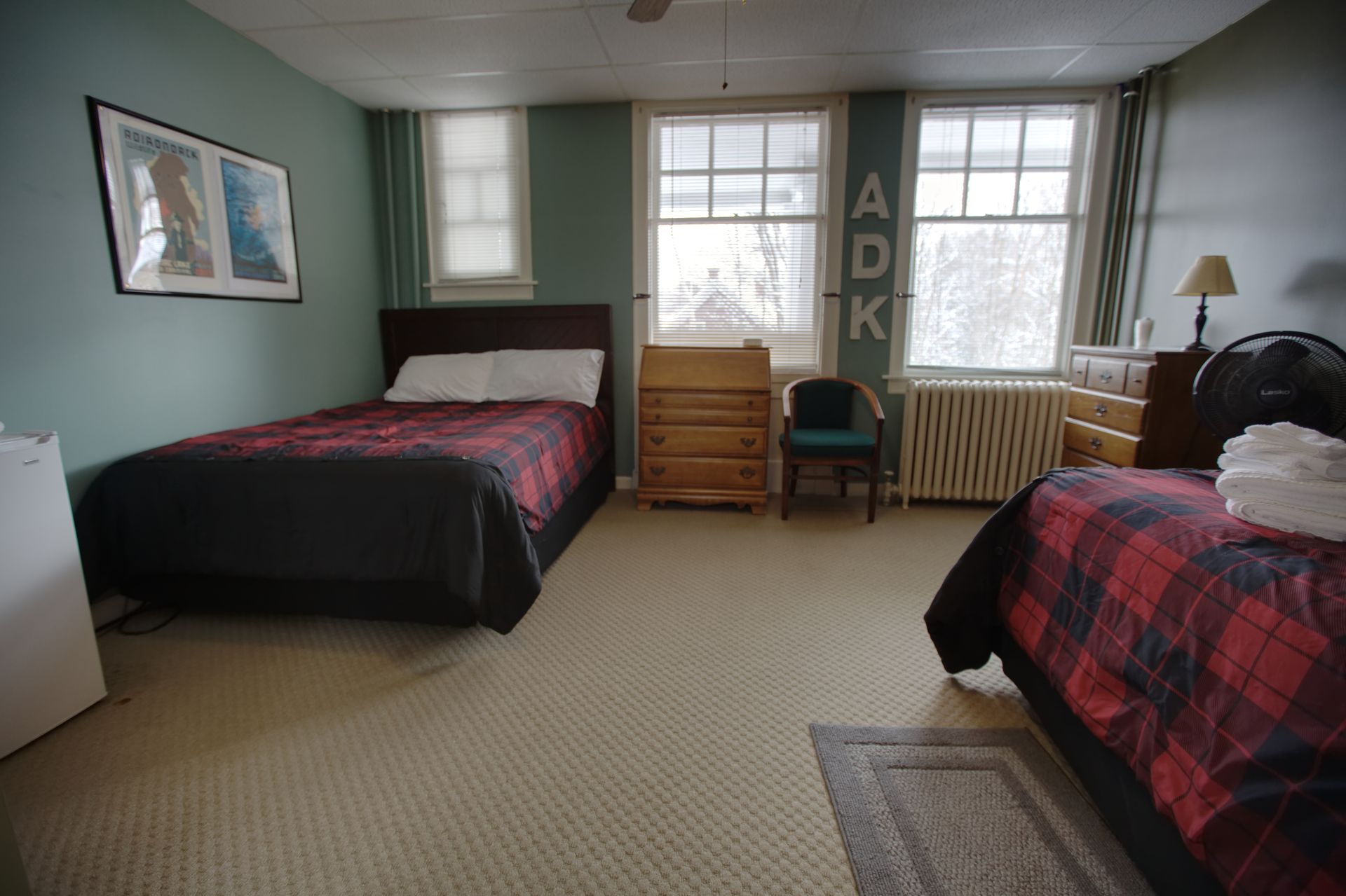 A bedroom with two beds a dresser and a fan