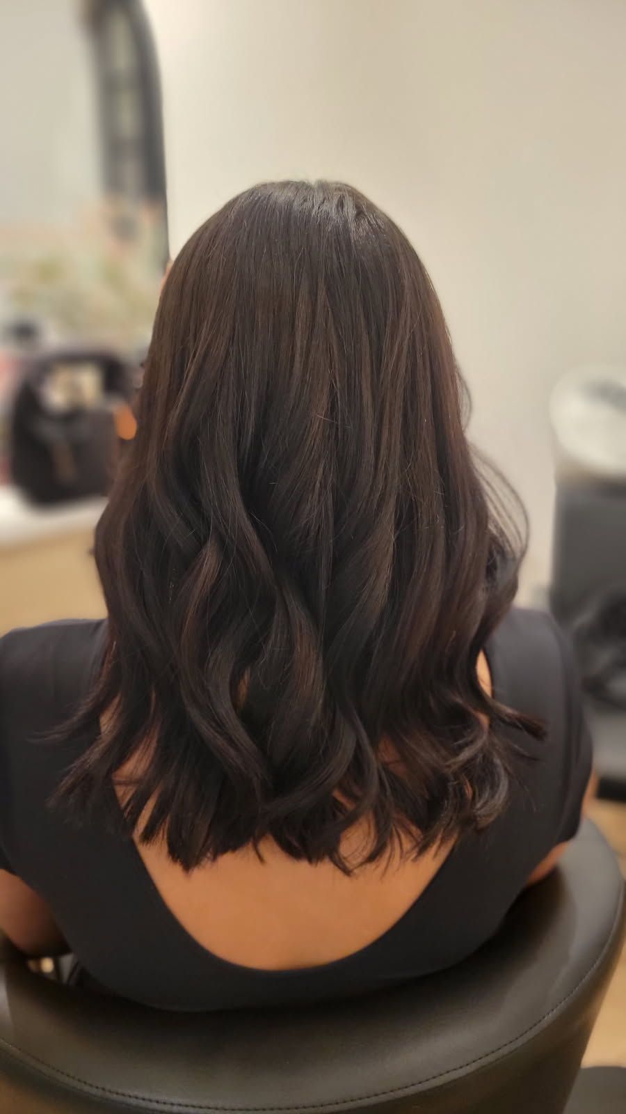 Dark wavy hair, styled in a bob, viewed from the back. Sitting in a chair in a salon.