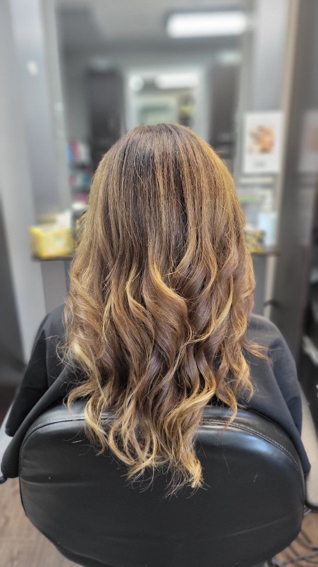 Back of a person's head, sitting in a salon chair; brown wavy hair with blonde highlights.