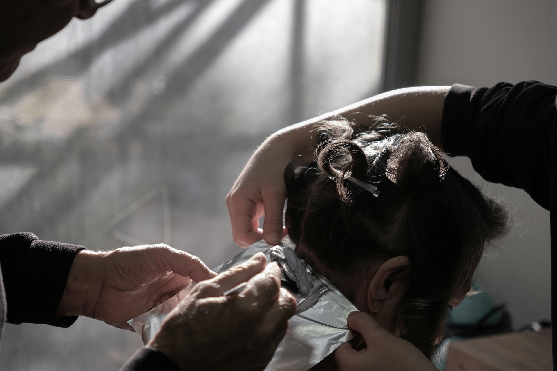 Person's hair being colored by two others. The hands are working with foils and clips.