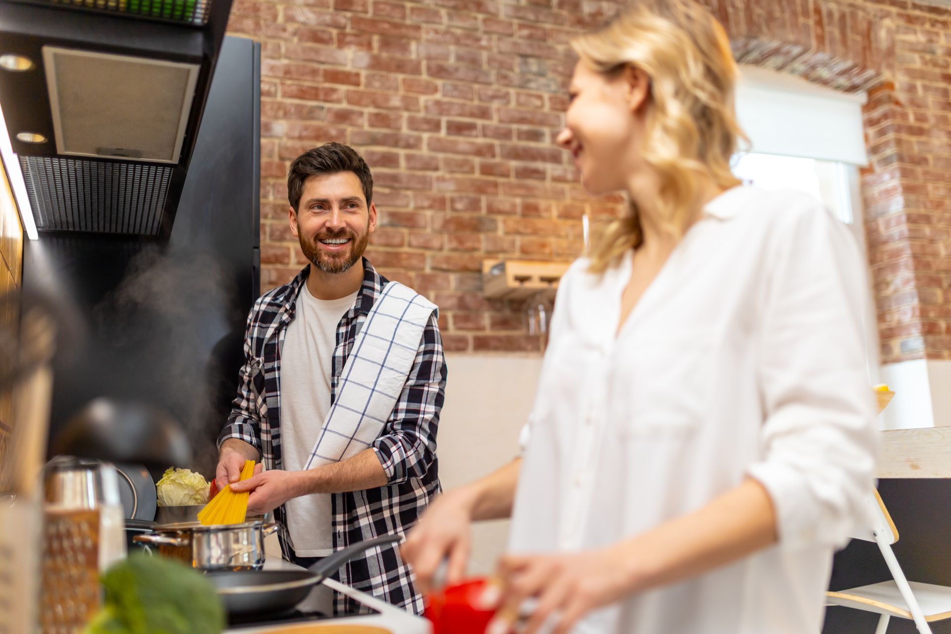 A young couple stands in their outdoor kitchen cooking a meal