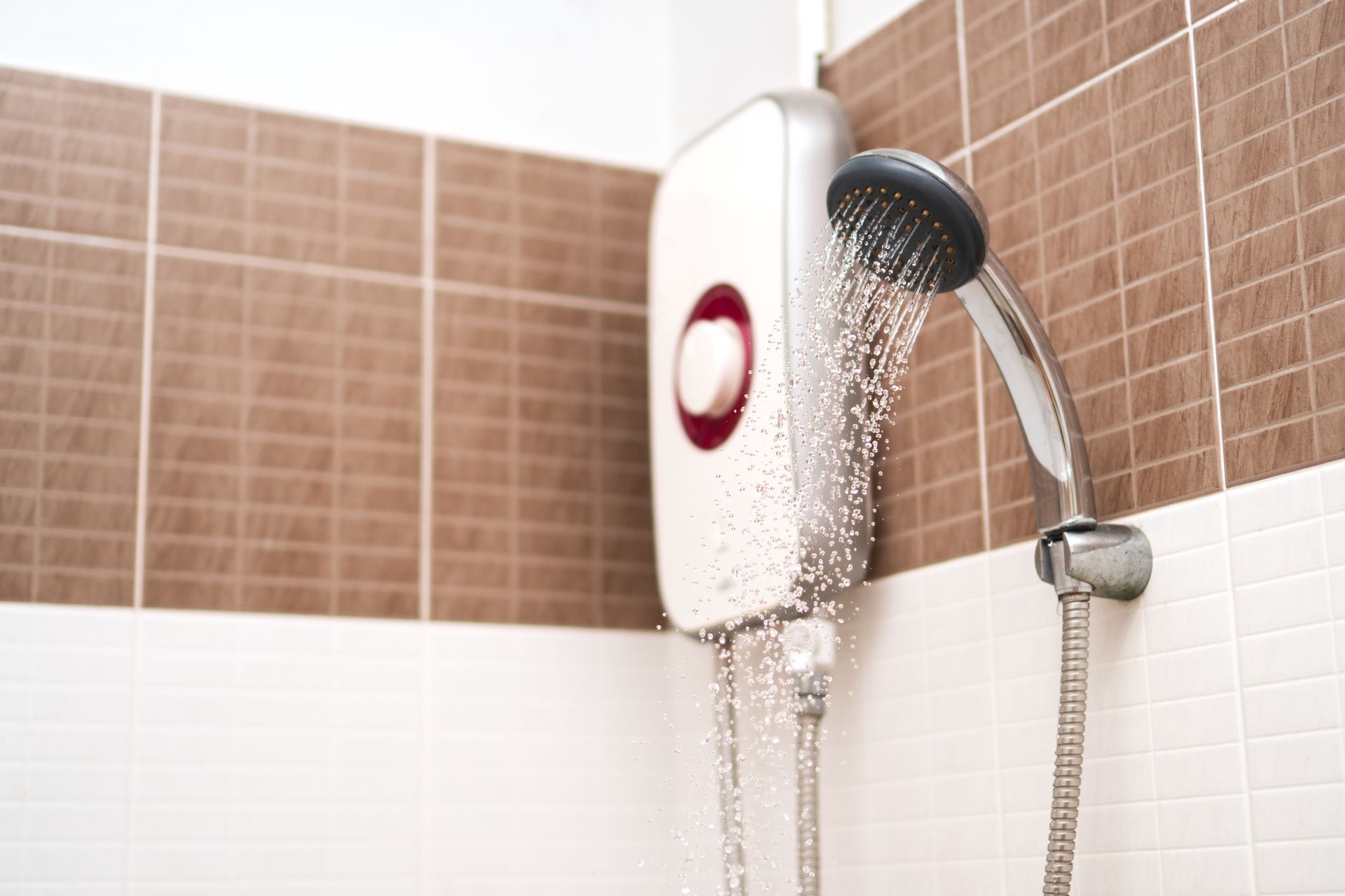 White and brown tiled shower with a white, electric water heater and a shower head. Water is running.