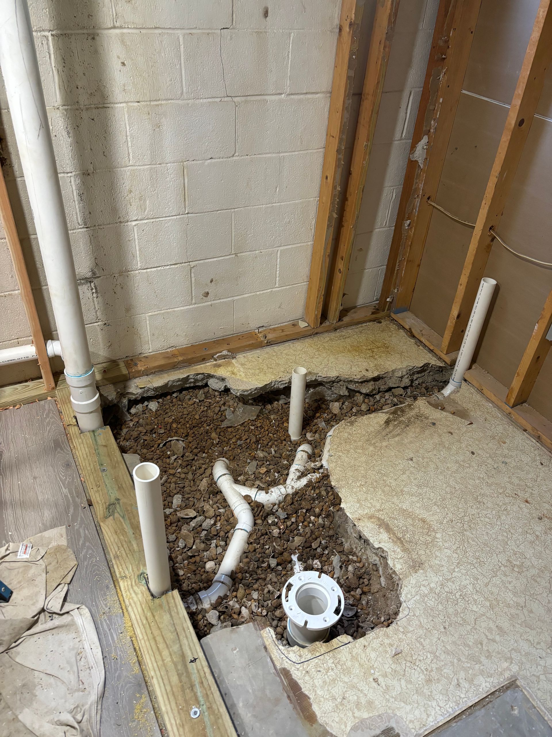 Bathroom plumbing rough-in. Open floor reveals pipes and drain, set in gravel base, within a framed wall.