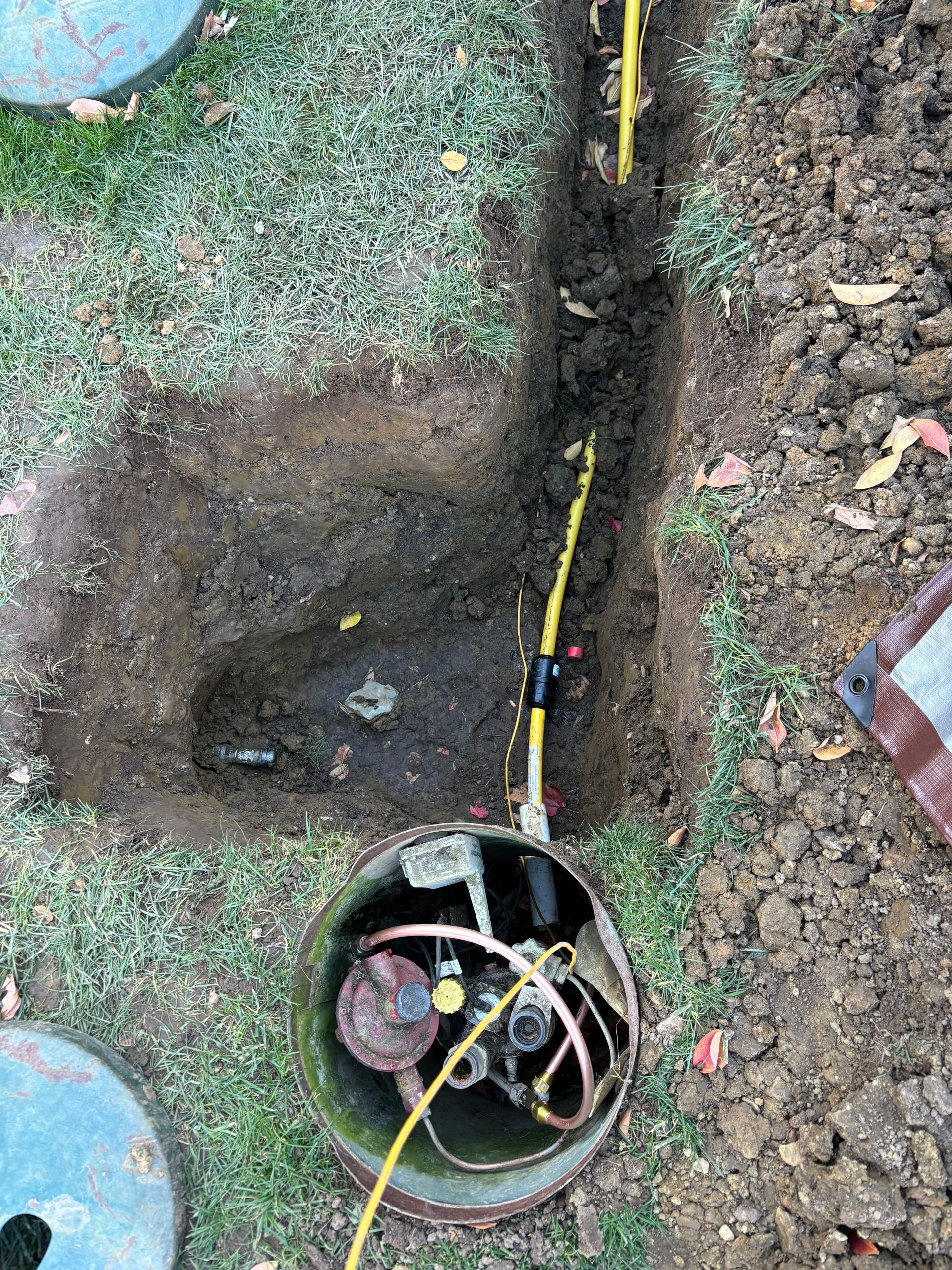 Open trench reveals gas meter and yellow gas lines in a yard.