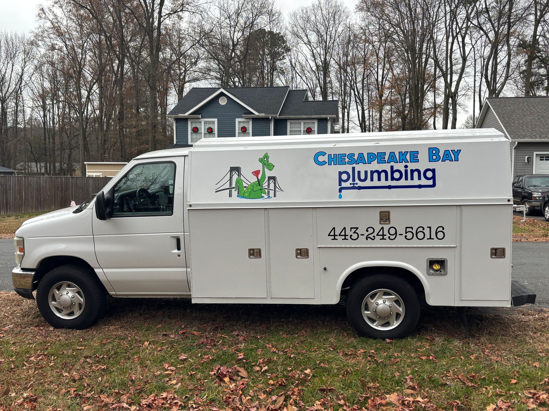 White Chesapeake Bay Plumbing service truck parked on grass. Building and trees in the background.