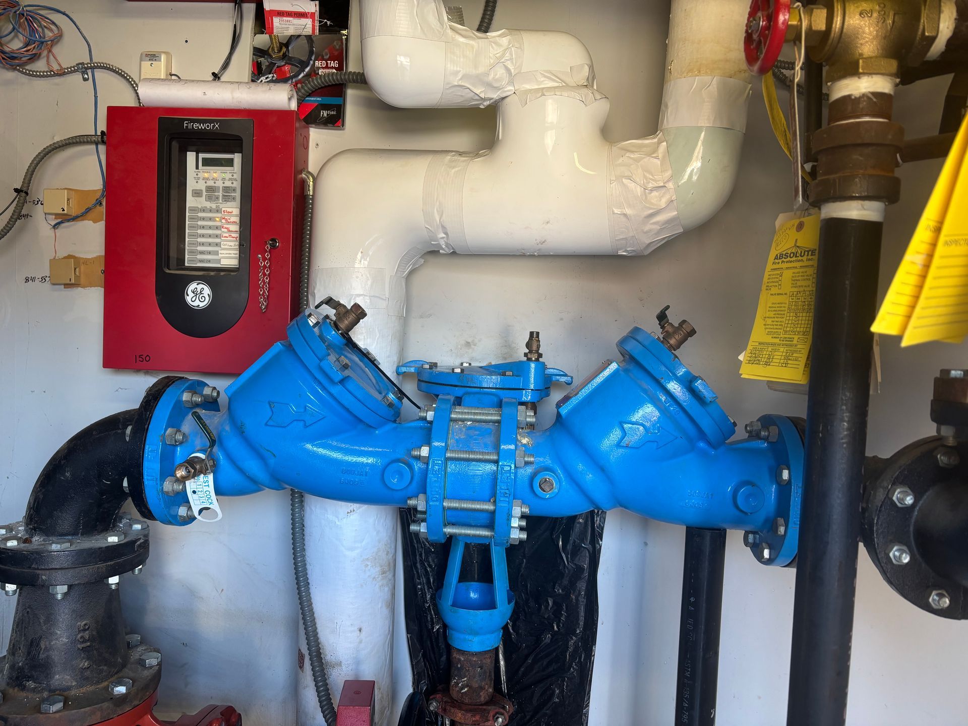 Blue and black water pipes with a red control panel and white insulated pipes in an industrial setting.