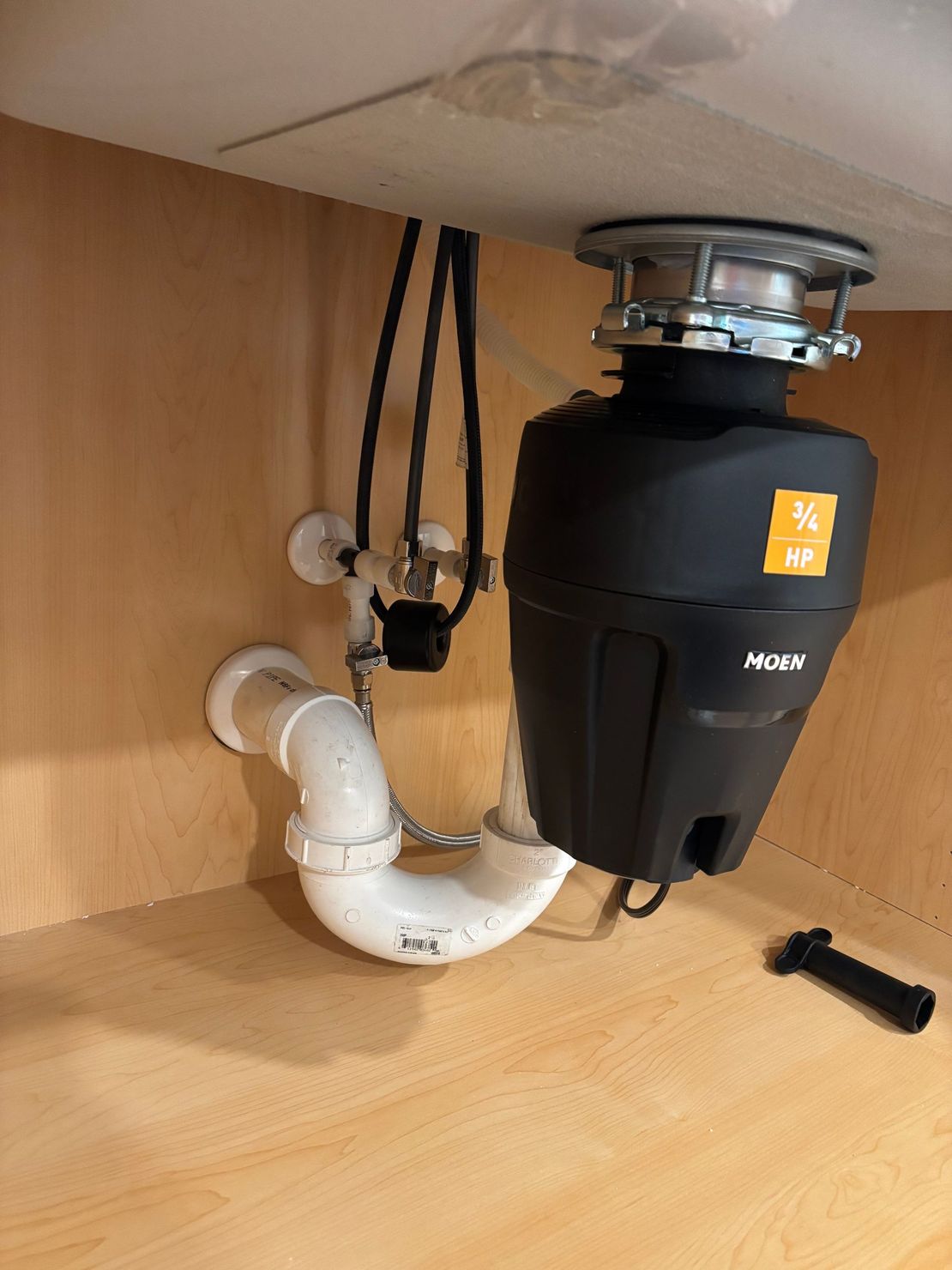 A kitchen cabinet with a Moen garbage disposal and connected plumbing.
