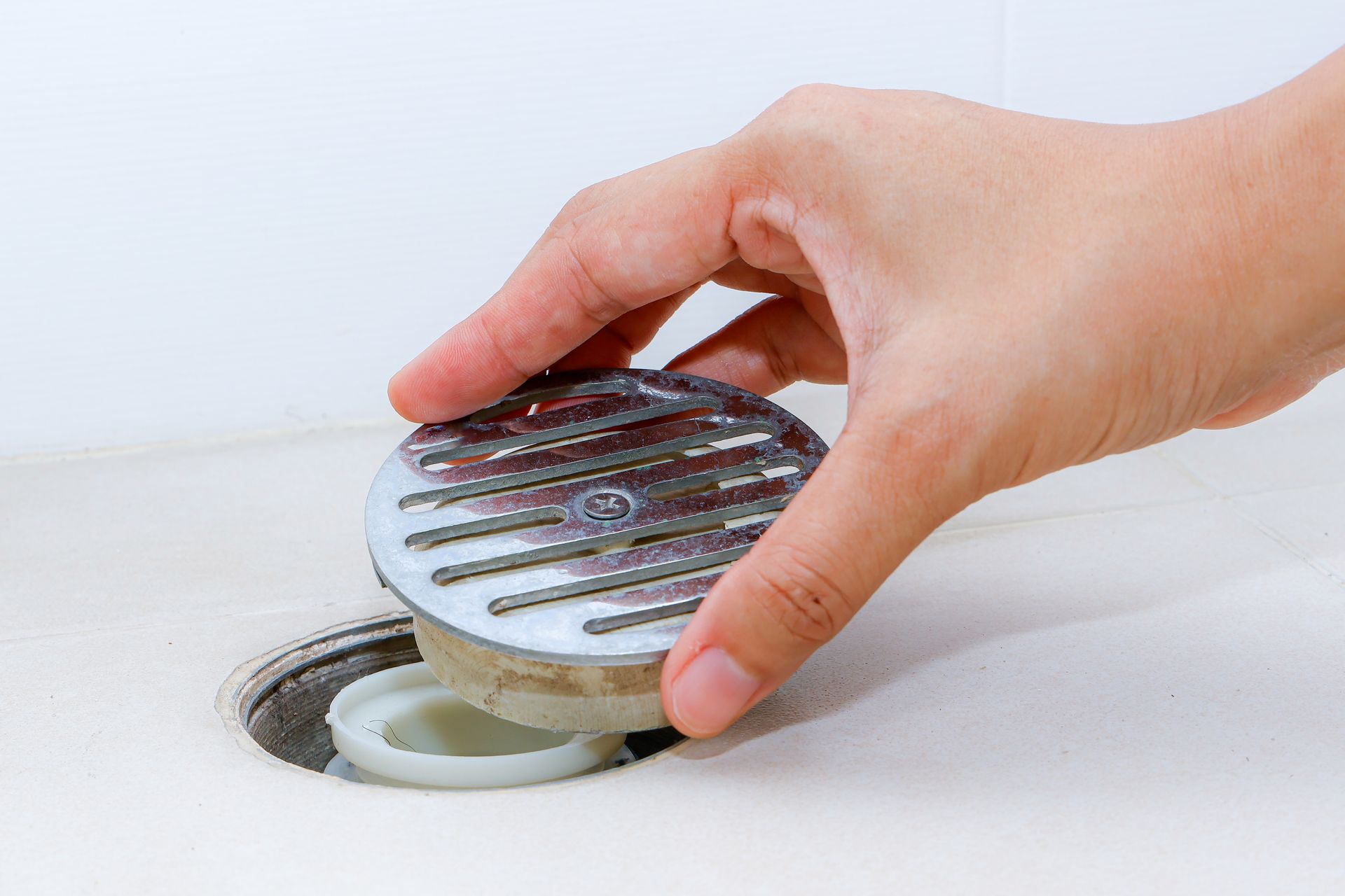 Hand removing a drain cover from a white sink.