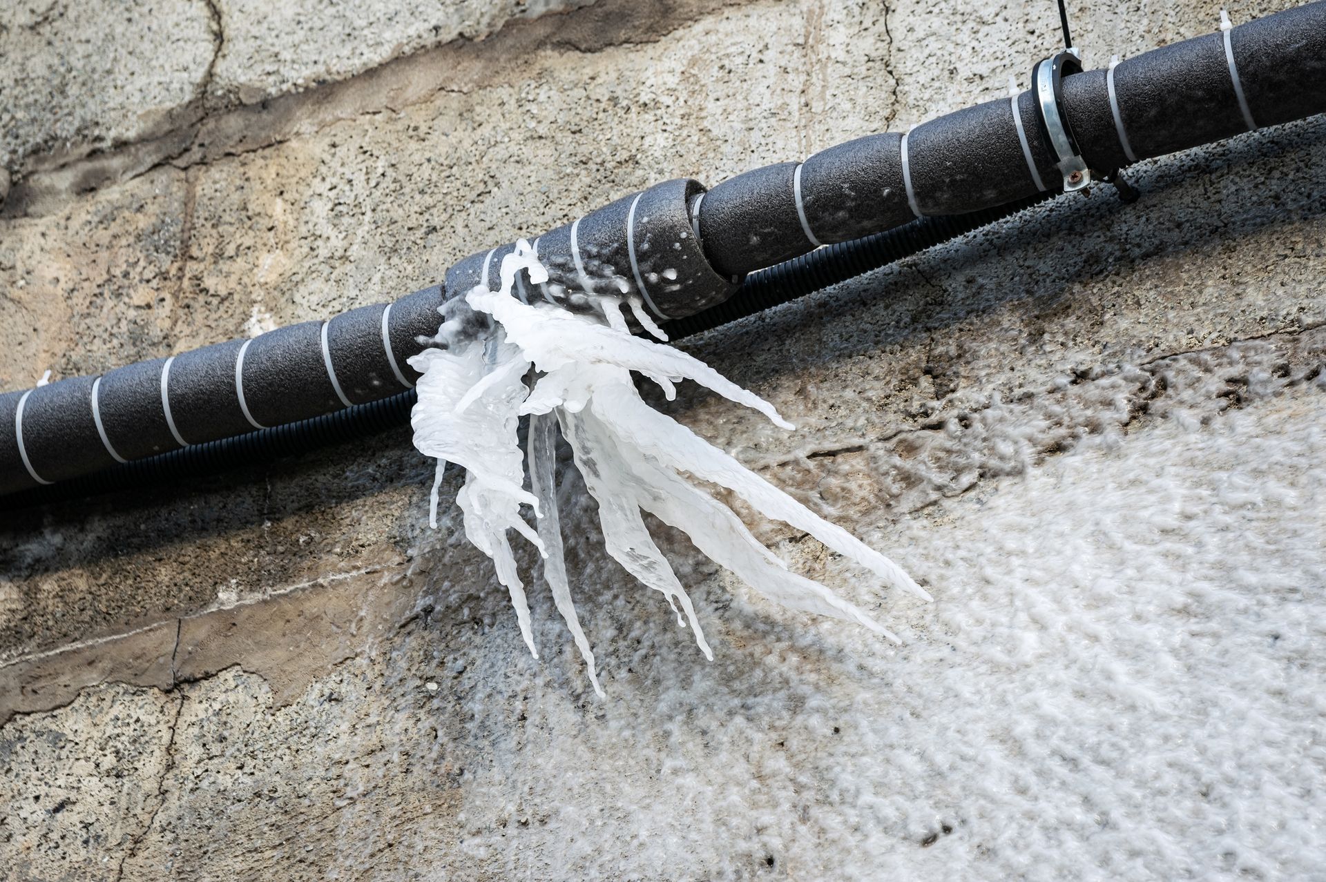 Frozen pipe with icicles on a concrete wall.
