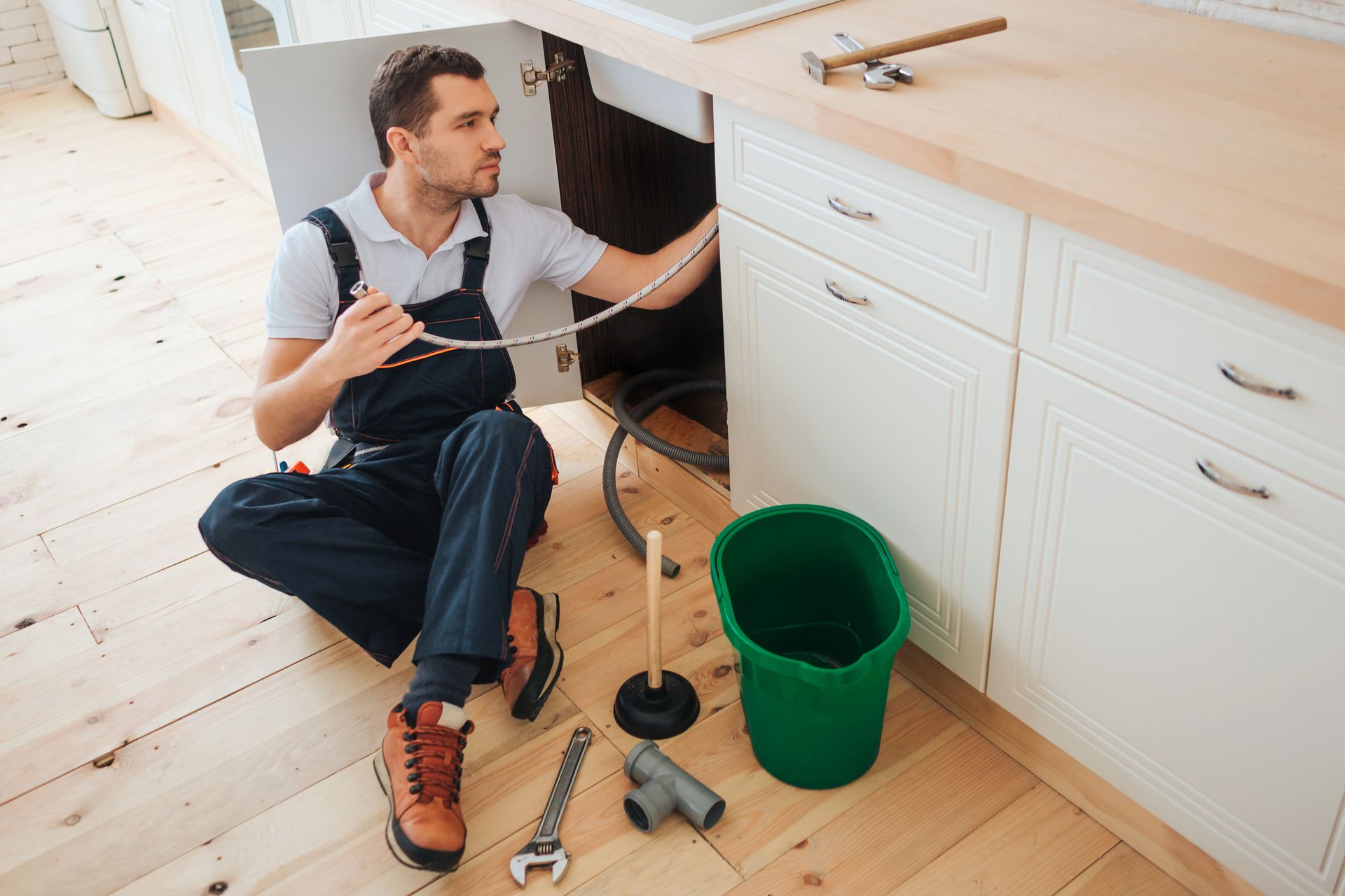 A plumber is kneeling on the floor fixing a sink in a kitchen.