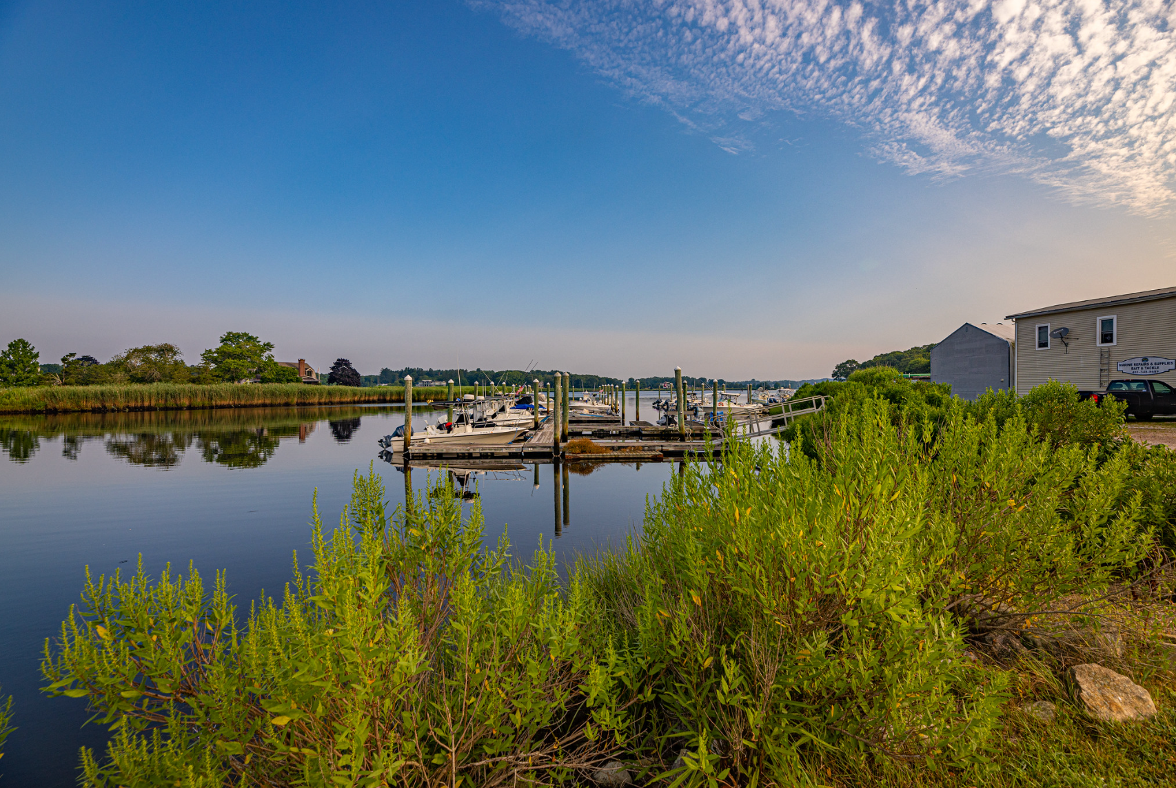 A dock with boats docked in the water and a house in the background.