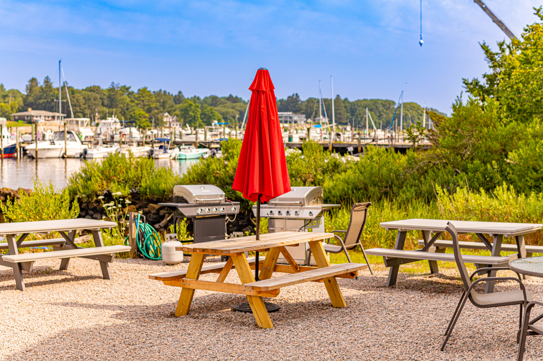 A picnic table with a red umbrella in front of a marina.