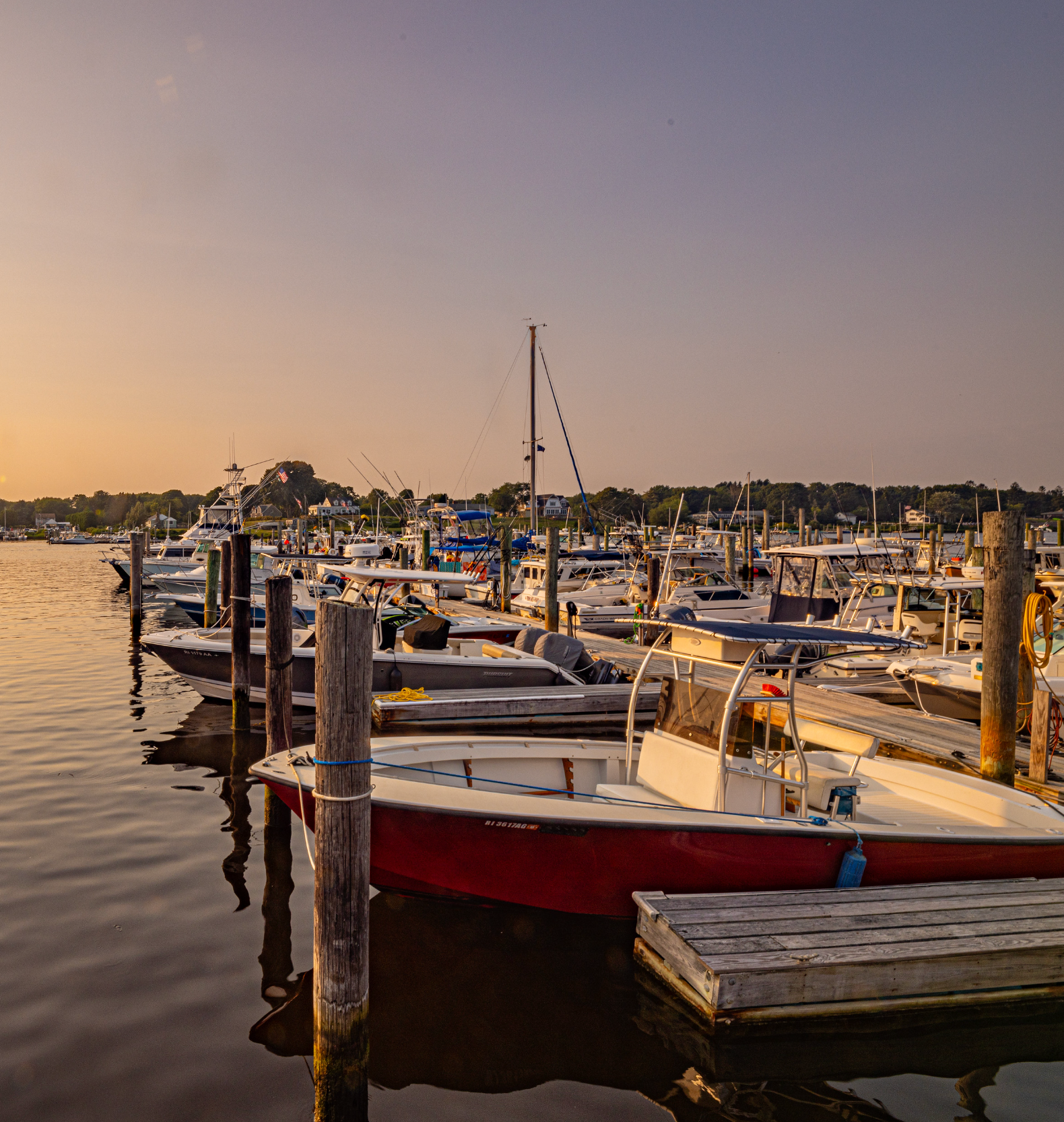 Many boats are docked in a harbor at sunset