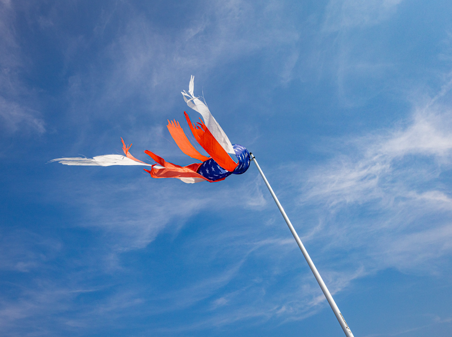 A red , white and blue flag is flying in the wind against a blue sky.