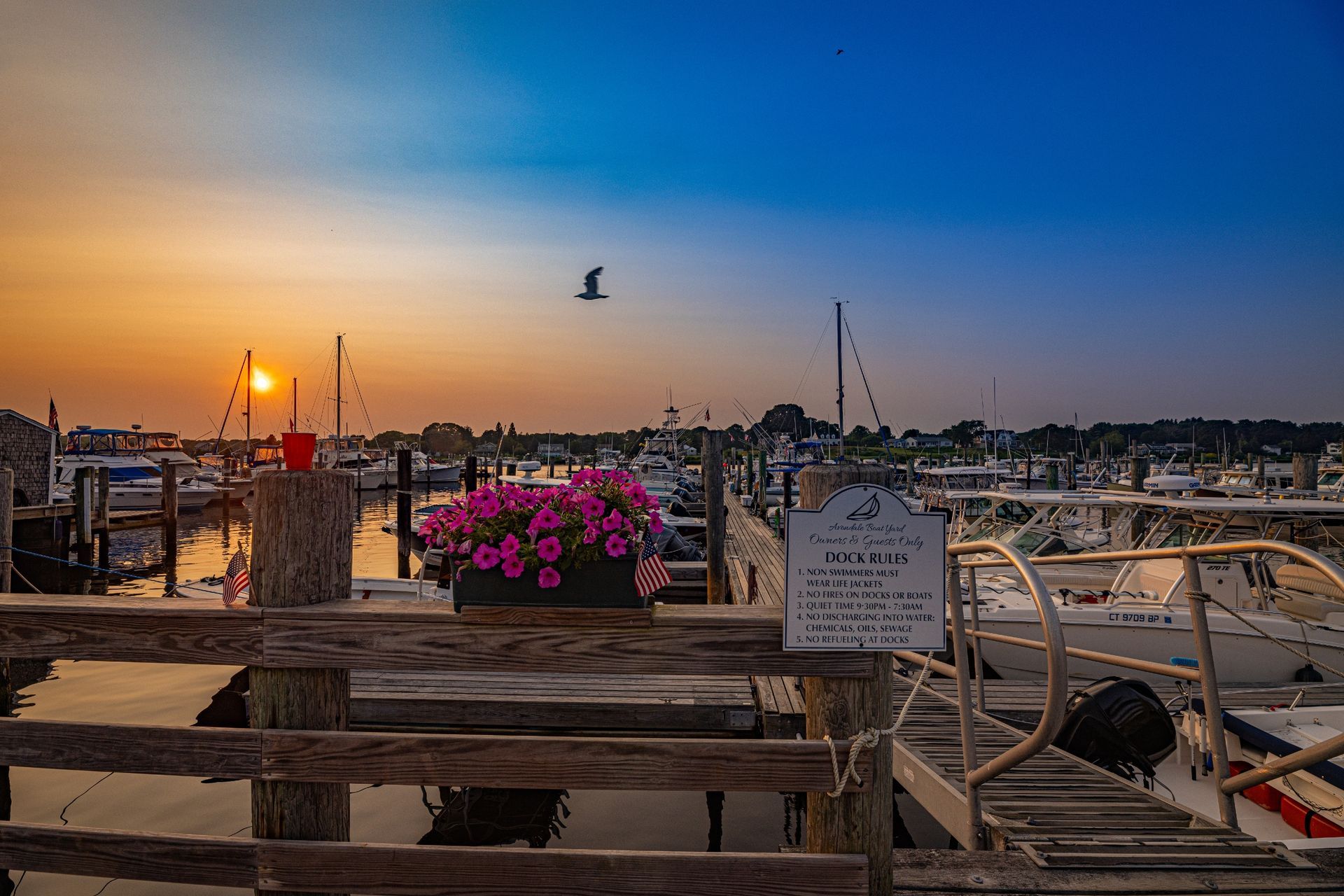 A wooden fence surrounds a marina with boats docked at sunset.