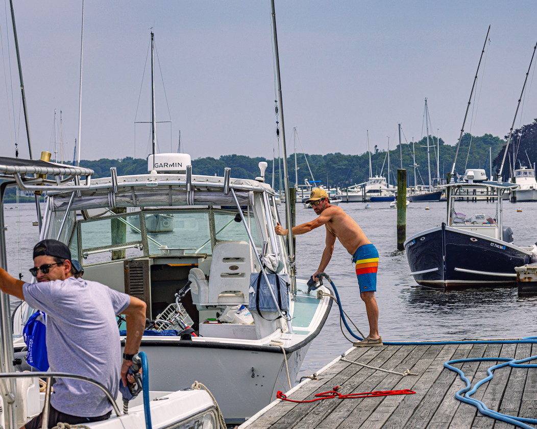 A man is washing a boat with a hose on a dock.