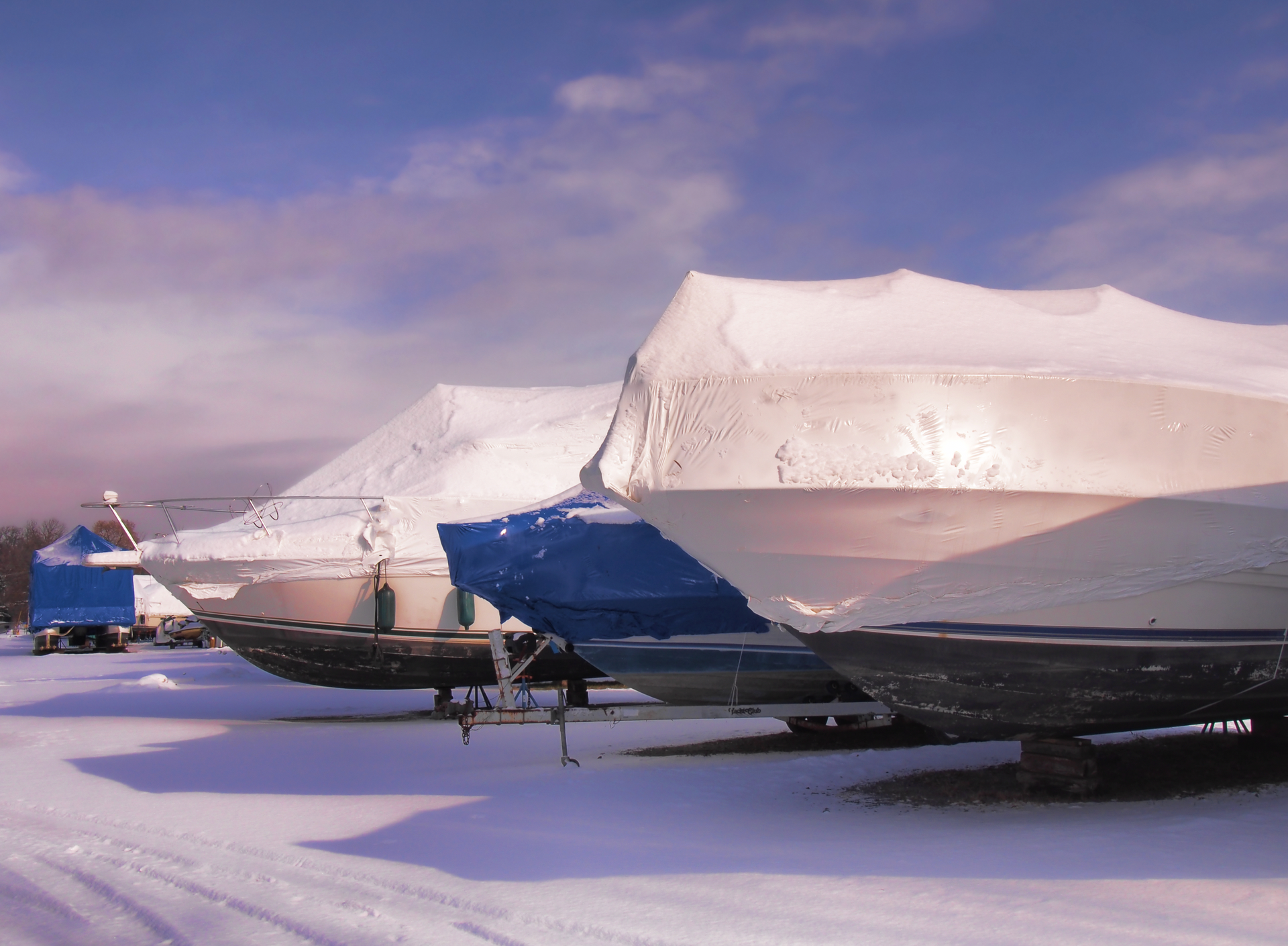 A row of boats covered in snow in a parking lot