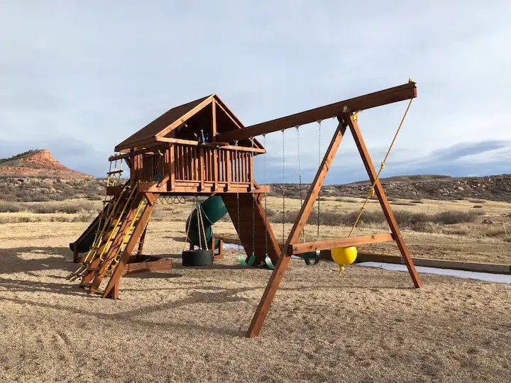 A wooden playground set with a slide and swings in a field.