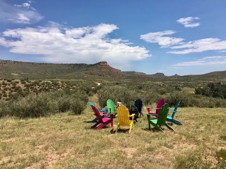 A group of colorful lawn chairs are sitting in a field with mountains in the background.