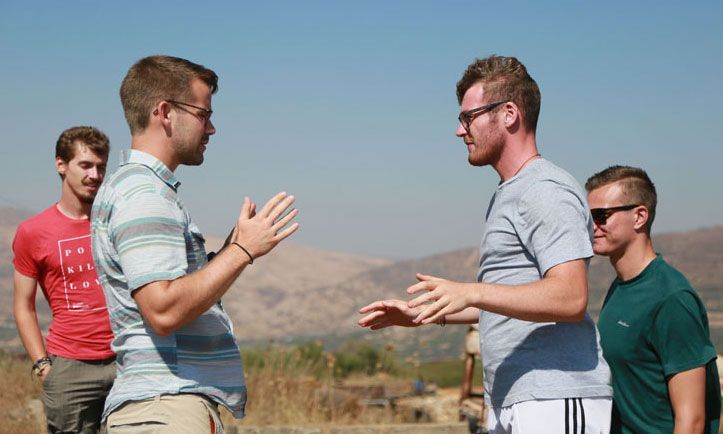A group of young men are standing in a field talking to each other.