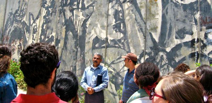 A group of people are standing in front of the separation wall with a painting on it.