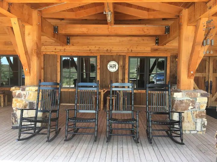 A row of rocking chairs are sitting on a wooden deck in front of a wooden building.