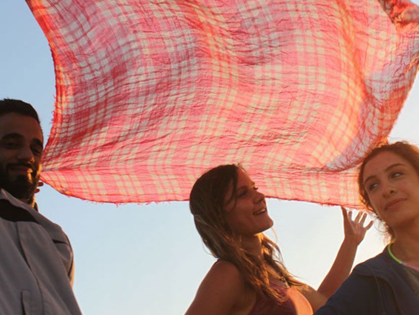A man and two women holding a red plaid scarf over their heads