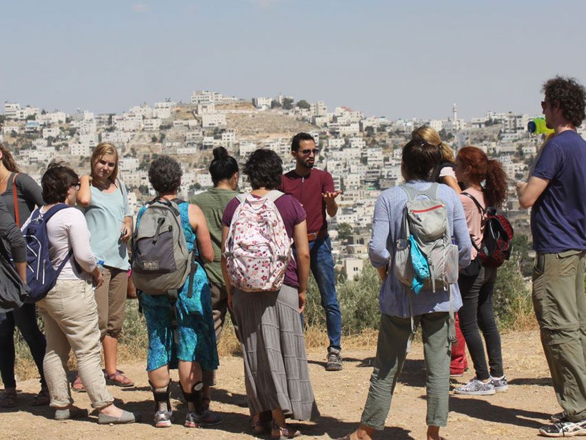 A group of people standing on top of a dirt hill looking at a city.