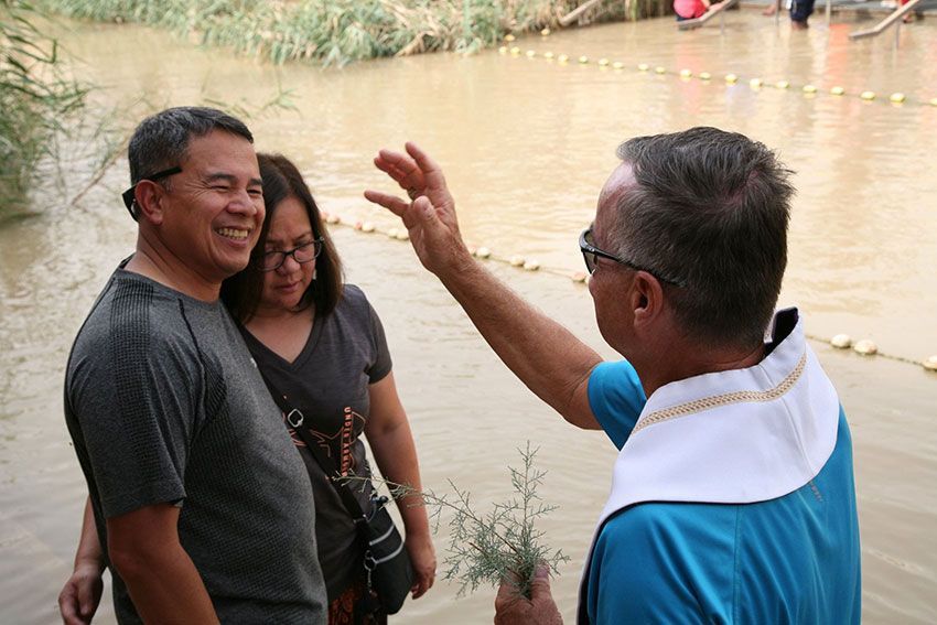 A man and a woman are being blessed by a priest in the Jordan River