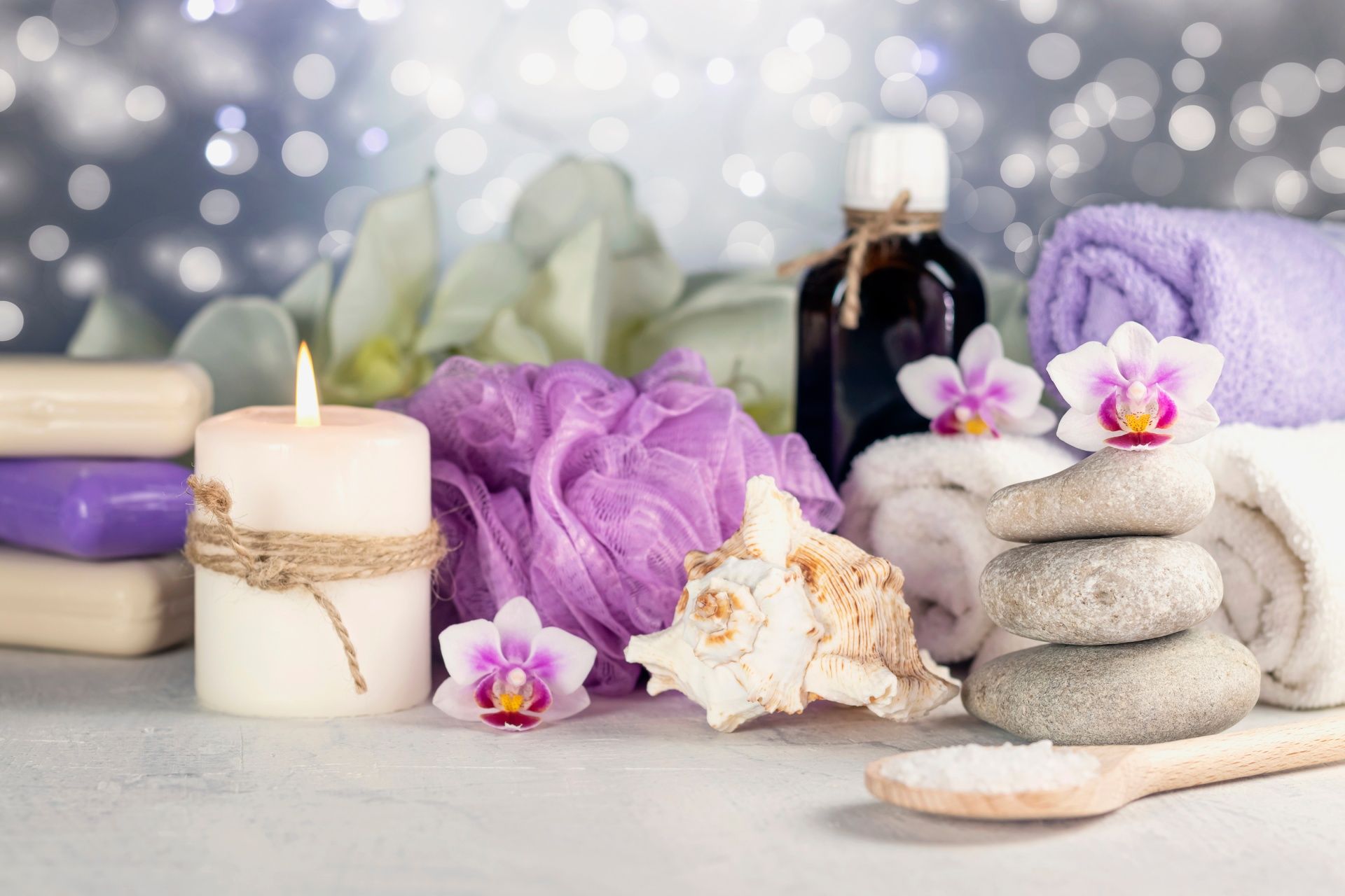 A spa setting with candles , towels , rocks , flowers and soap.