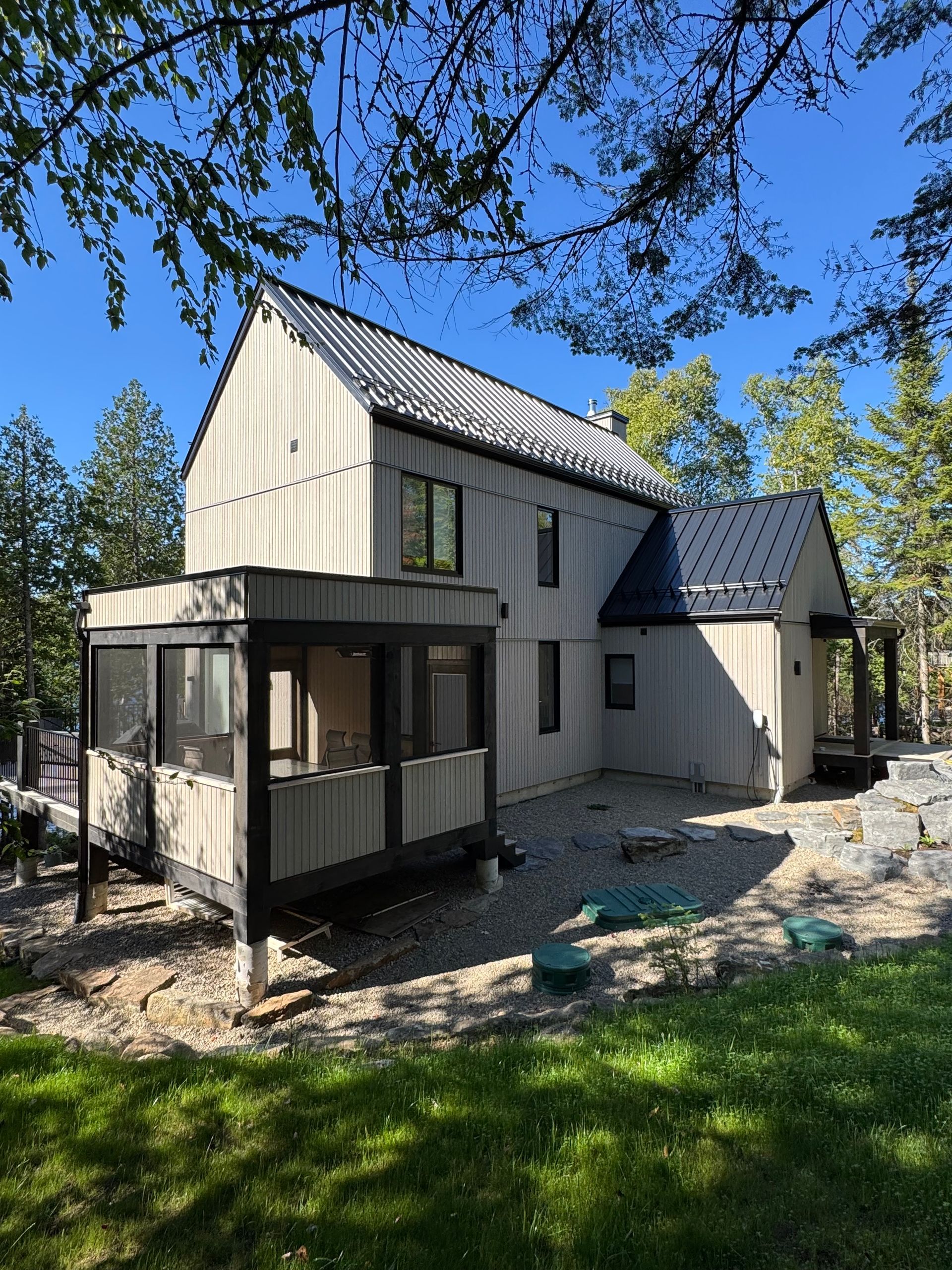 Maison moderne à deux étages avec toit et bardage en métal, véranda grillagée, nichée dans un cadre boisé.