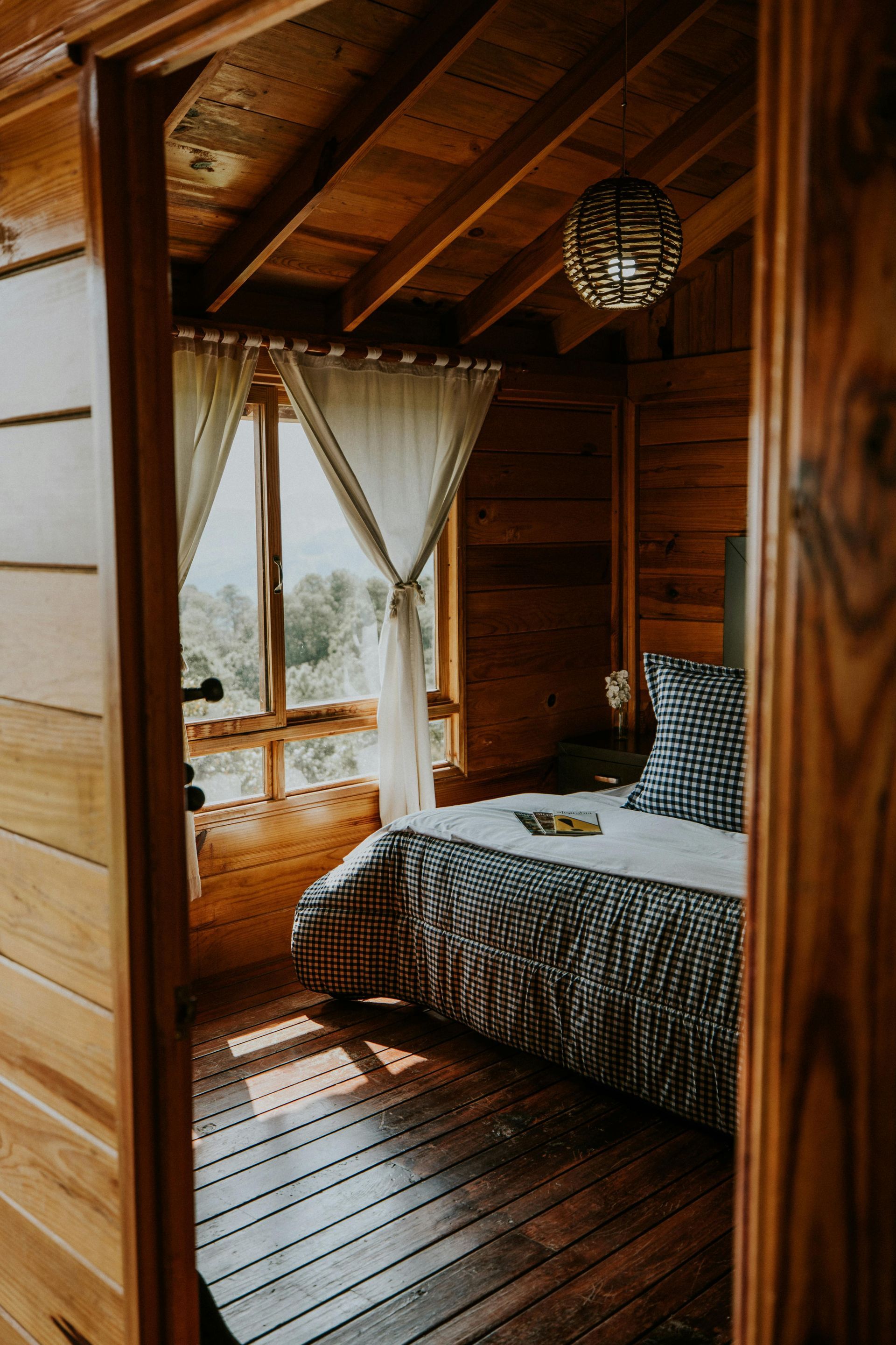 Chambre en cabane de bois avec lit, fenêtre et luminaire suspendu.