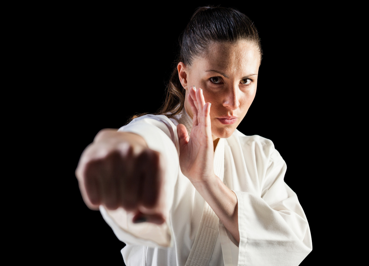 A woman in a white karate uniform is making a fist in the air.