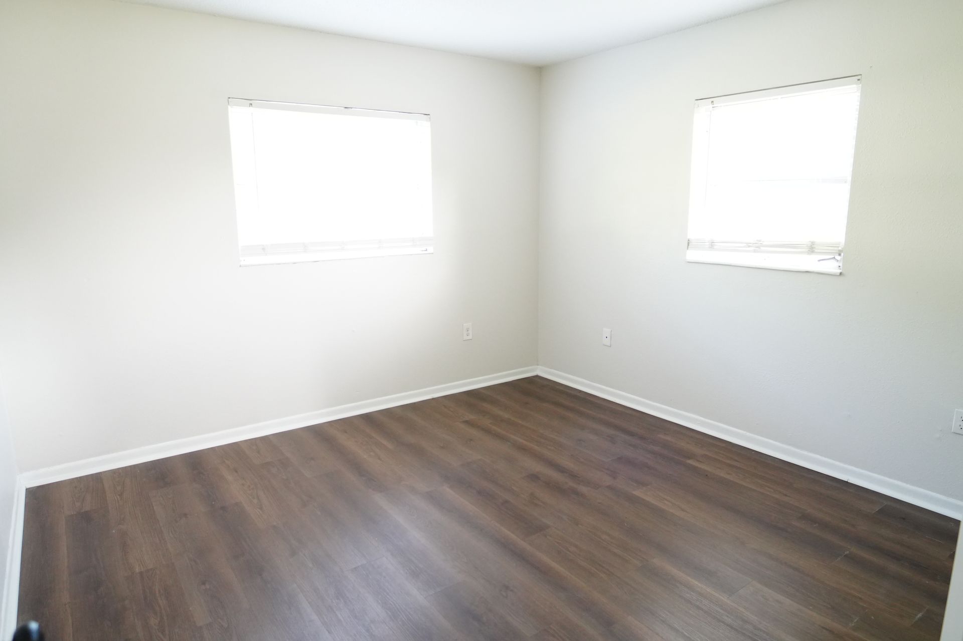 An empty bedroom with hardwood floors and two windows.