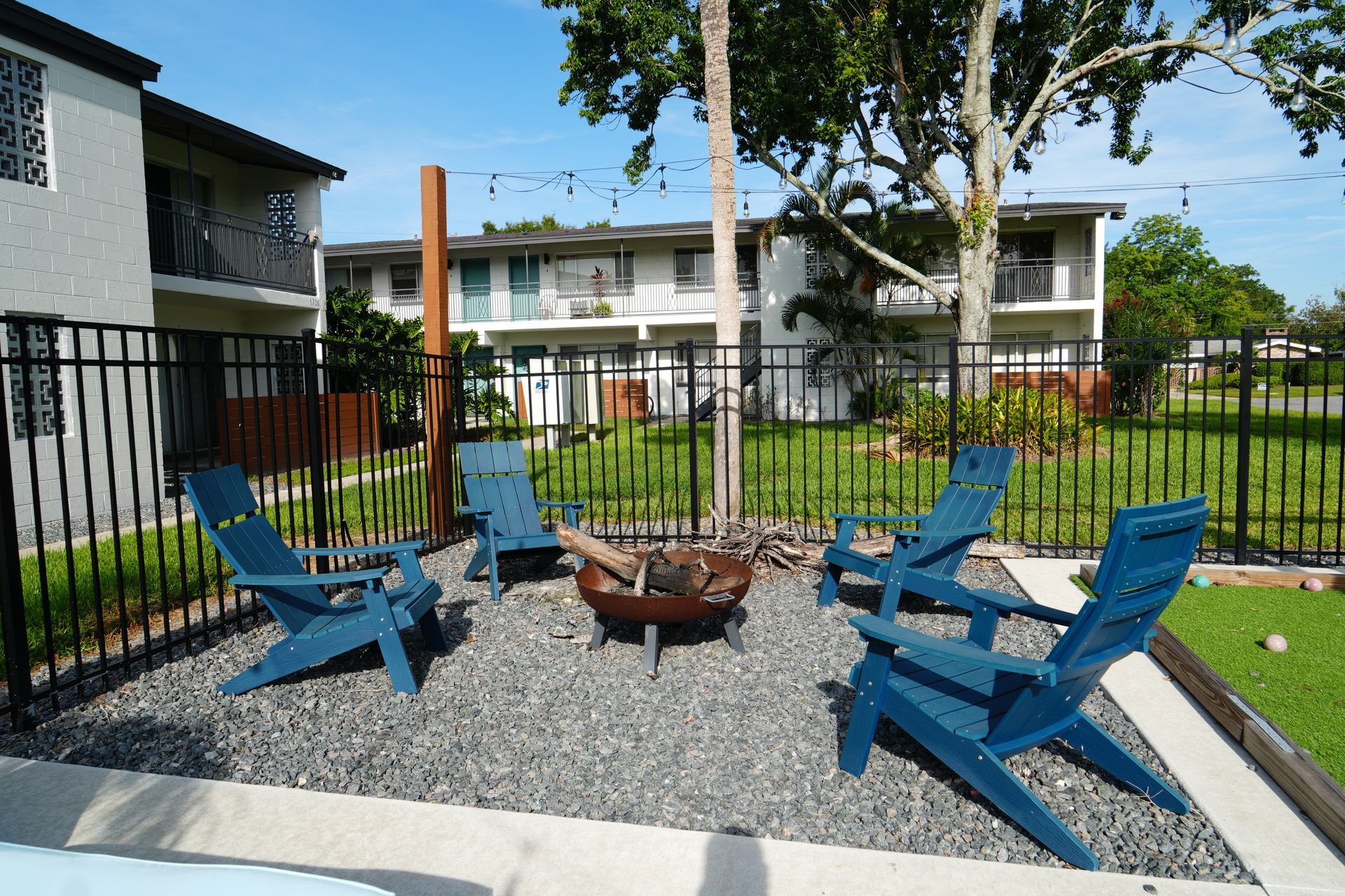 A fire pit surrounded by blue chairs in front of a fence