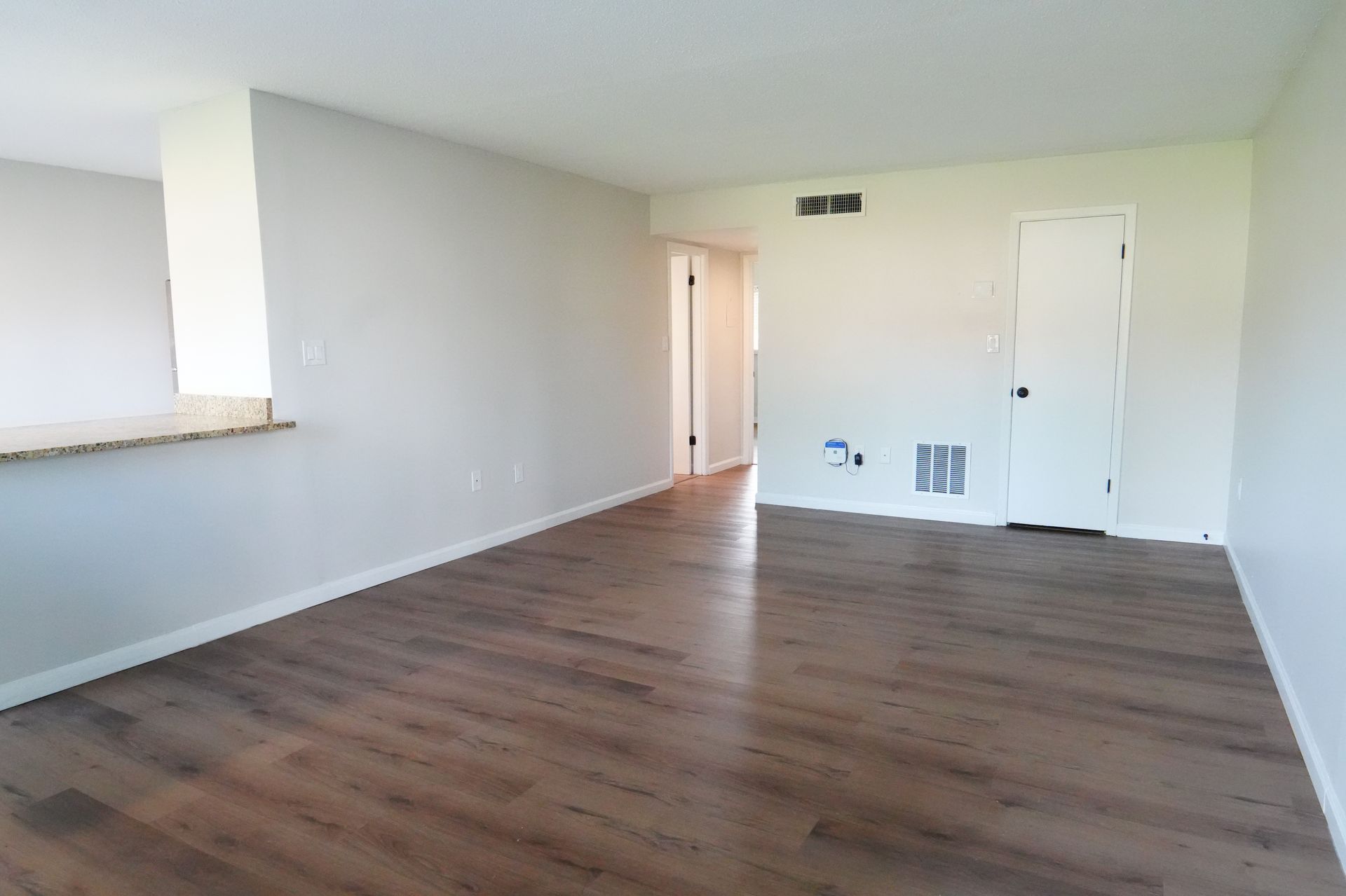 An empty living room with hardwood floors and white walls.