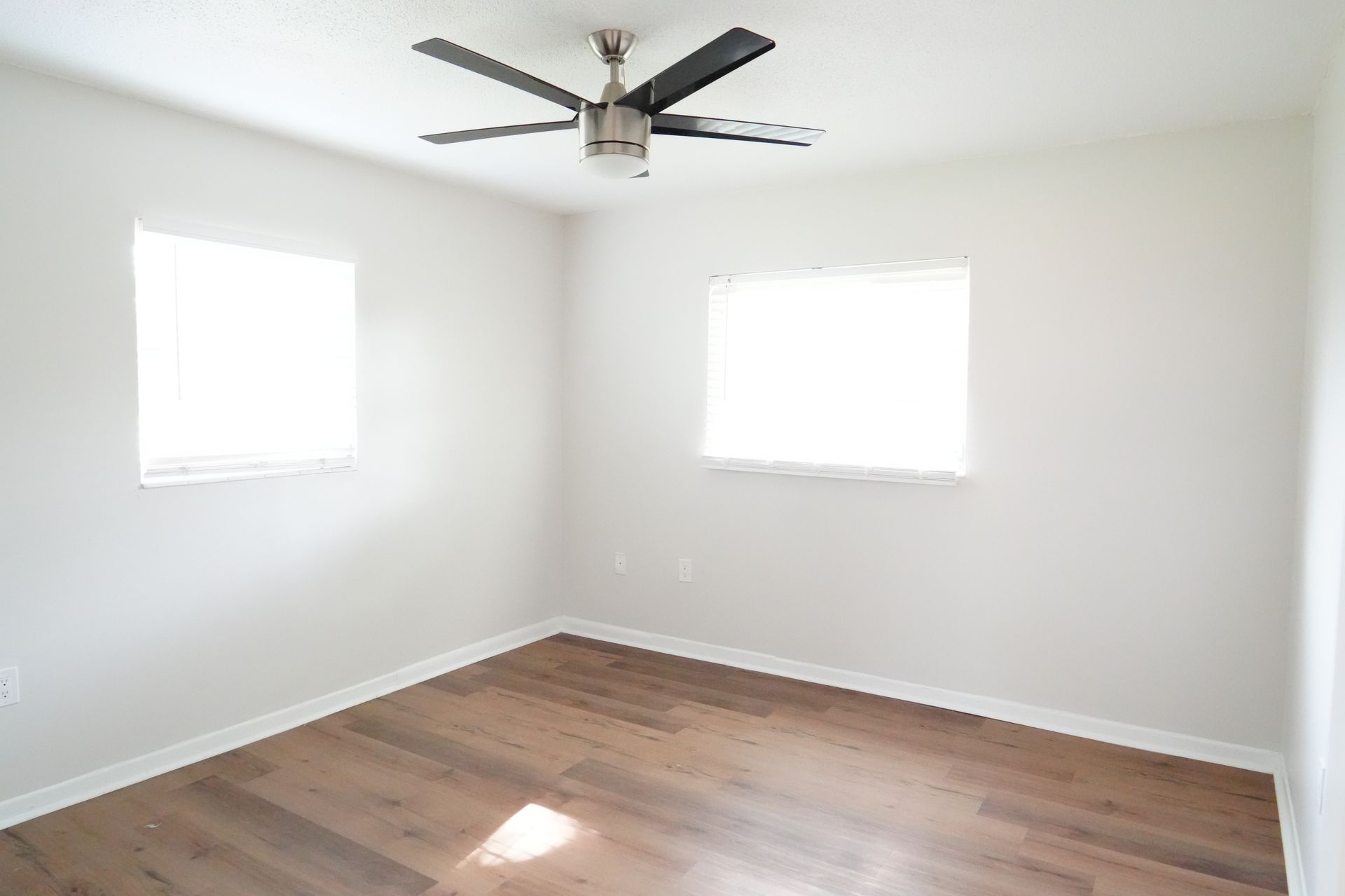 An empty room with a ceiling fan and two windows.