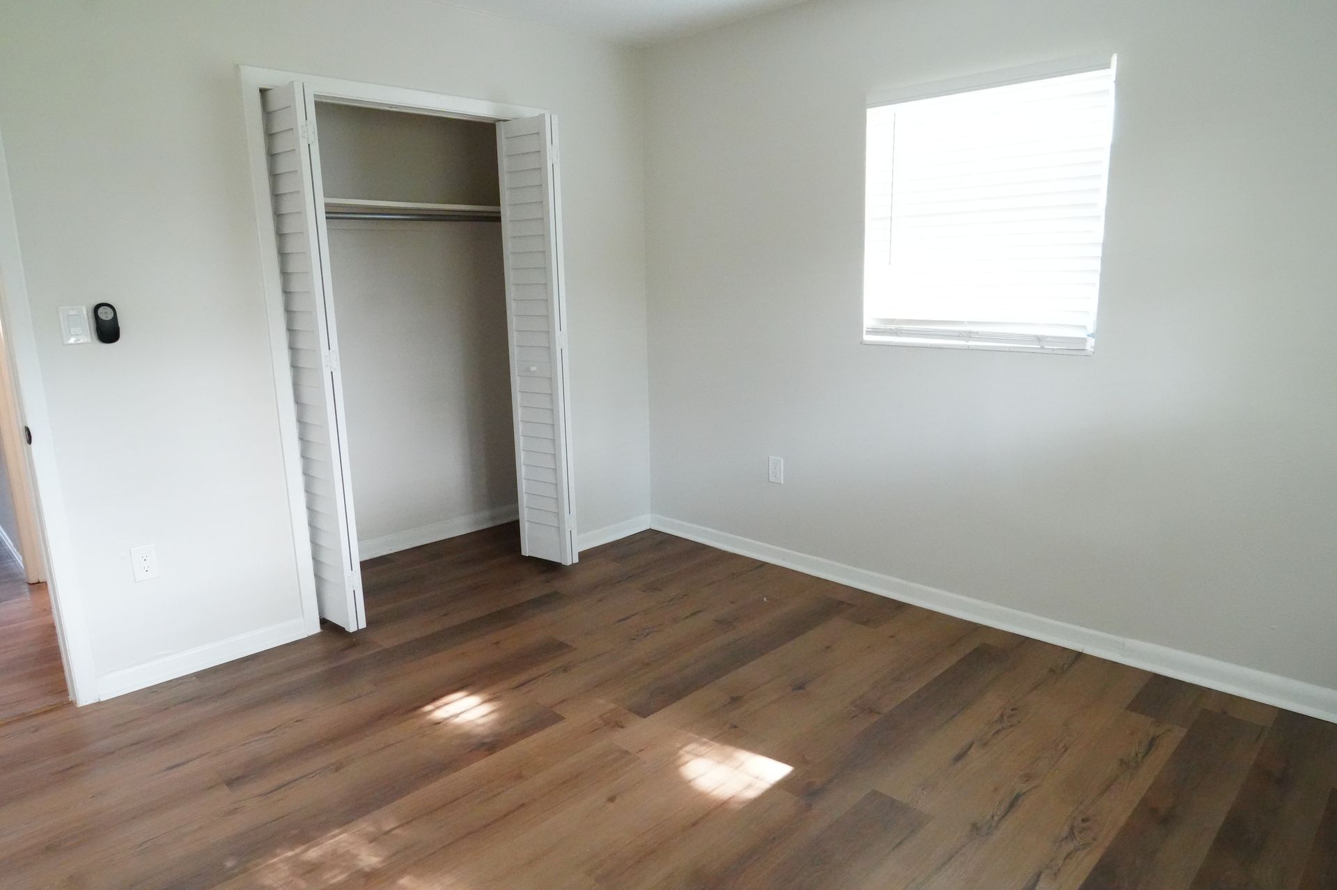 An empty bedroom with hardwood floors and a closet.